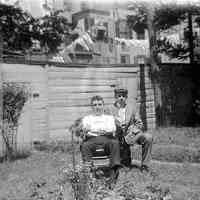 B+W negative image of an unidentified man and a teen boy seated in a backyard, no place, no date, ca. 190