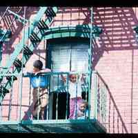 Color slide of three children on the fire escape of a brick building.