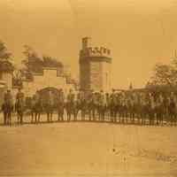 Sepia-tone photo of Hoboken Riding Club members on horseback in front of Stevens Gatehouse, 6th St. and Castle Point, ca. 1904.