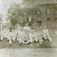 Sepia-tone photo of group of men posed outdoors on grass with fence & building behind, Hoboken?, n.d., ca. 1905-1910.