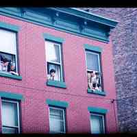 Color slide of people looking out of the windows of a brick building.