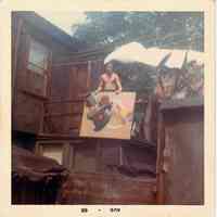 Color photo of a man on a rear deck of a Willow Terrace house holding a painting, Hoboken, August 1966.