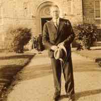 Digital image of photo of man in suit holding his hat standing outside a St. Joseph