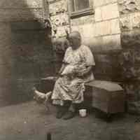 Digital image of B+W photo of Pasqualina Gallo seated on a bench holding a chicken in backyard of 509 Monroe St., Hoboken, no date, ca. 1920-1930.