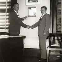 Digital image of b+w photo of Mayor Fred DeSapio putting up first Civil Defense poster with Philip Morris manager, Hoboken, no date, ca. 1950-1952.