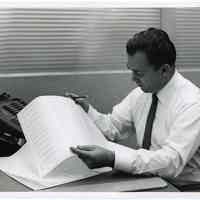 B+W photo of Peter (Alvin P.) Roland working at a desk, Hoboken, n.d., ca. 1960-1970.