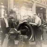 Image: Four men working on a turbine compresser shaft with two men overseeing them, no place, no date, ca. 1931-40.