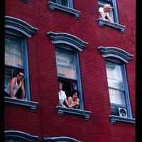 Color slide of people looking out of the windows of a brick building.