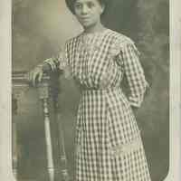 Photo postcard of an unidentified woman in checked dress posing in an unknown studio, no place, 1912.