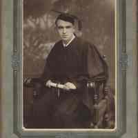 Sepia-tone photo of an unidentified man in graduation cap and gown holding a diploma in a seated pose, Hoboken, no date, ca. 1900-1910.