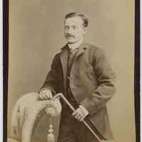 Cabinet photo of man with walking stick posed in photographer