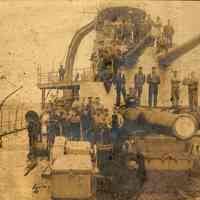 Sepia tone photo of shipyard workers posed on deck guns of unidentified naval vessel at Bath Iron Works, Bath, ME. No date, ca. 1905-1906.