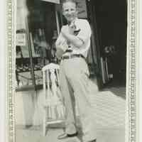 B+W photo of a man holding a cat posed in front of the exterior of Baron