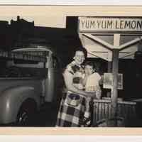 Digital image of b+w photo of a Aunt Rose holding a young child near a Yum Yum cart with truck, 416 Clinton St., Hoboken, n.d., ca. 1950s.