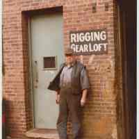 Color photo of Charlie Kosbab standing under the sign, Rigging Gear Loft,at the Bethlehem Steel Shipyard, Hoboken Division, ca. 1980.