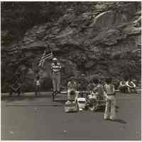 B+W photo of a group of people assembled on River Road, one man holding a flag, Hoboken, no date, [1976].