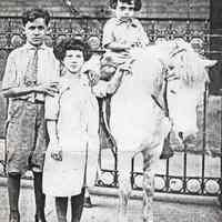 Black-and-white photocopy of photo of Frank Ratti, Mary Ratti and Anthony Ratti with a pony outside School No. 8, 700 Adams St., Hoboken, 1925.