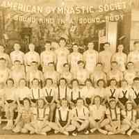 Sepia-tone group photo of American Gymnastic Society members posed in front of a stage at unknown place, probably in Hoboken, April 23, 1938.