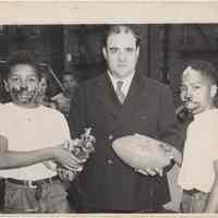 B+W photo of a man presenting prizes to 2 winners in a pie eating contest, Hoboken, no date, circa 1945-1950.