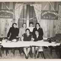 B+W photo of 6 women at trestle table with John Palumbo