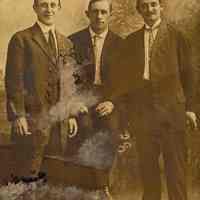 Sepia-tone photo postcard of 3 young men posed in photographer
