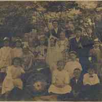 Sepia-tone photo of woman with children at festival with Maypole & patriotic decor, n.p. (Hoboken?), n.d., ca. 1905-1920.