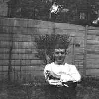 B+W negative image of an unidentified man seated in a backyard holding a cigar, no place, no date, ca. 190