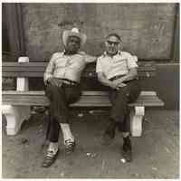 B+W photo of two men seated on a city bench near a boarded-up window, Hoboken, no date, [1976].