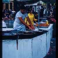 Color slide of a man making food at a street fair.