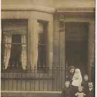 Photo postcard of woman holding baby plus three young girls and a boy on front steps of unidentified building, probably Hoboken, no date, ca. 1910.