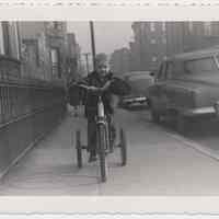 B+W photo of George Miller on a tricycle near Twelfth St. & Park Ave., Hoboken, n.d., ca. early 1950s.