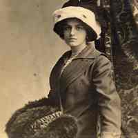 Digital image of photo postcard of a young woman posed with cloth coat, hat & fur trimmed muff, Jersey City, no date, circa 1900-1915.