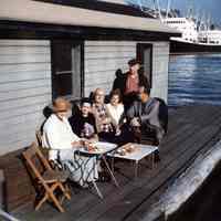 Color photograph of a group seated on the floating shack docked at 4th St. & Hudson River, Hoboken, n.d., ca.1970s.