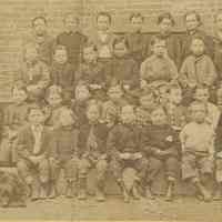 Sepia-tone group photo of schoolboys with priest outside what is probably the school building, no place, no date, ca. 1900.