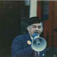 Digital image of color photo of Tom Vezzetti with electric megaphone wearing American Legion Post 107 cap, Hoboken, no date, circa 1980-86.