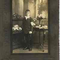 Sepia-tone photo of young boy holding rosary & catechism posed in studio, Hoboken, n.d., ca. 1900-1920