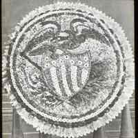 Lantern slide, b+w, of floral decoration with eagle and patriotic shield motif, used for promotional display in Hoboken, no date, ca. 1920.