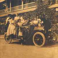Digital image of sepia-tone photo of eight women, two girls and boy on the Muller family car outside a hotel or inn, no place, no date, ca. 1910-20