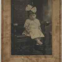 Sepia-tone photo of an unidentified young girl, ca. 2 years old, seated in a chair in photo studio, Hoboken, no date, ca. 1900.