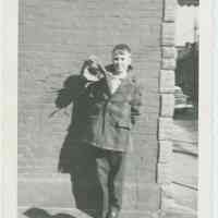 B+W photo of a boy(?) leaning against a wall & holding a doll on Clinton Street near Willow Terrace, Hoboken, [1959].