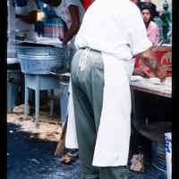 Color slide of a man making food at a street fair.