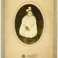 Sepia tone photo of a young girl in white dress holding flower, Hoboken, n.d., ca. 1915-1925.