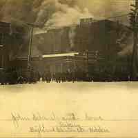 Sepia-tone photo of exterior view of a fire on the Clinton & Eighth Sts. corner of John Schmalz