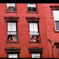 Color slide of people looking out of the windows of a brick building.