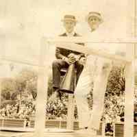 Digital image of photo of two men on platform, one with megaphone, audience stands behind them, no place, no date, ca. 1910-1920.