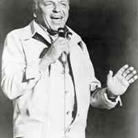 Black-and-white photo of Frank Sinatra in performance wearing a leisure suit, no place, no date, ca. 1975.