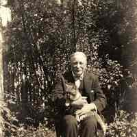 B+W photo of of Richard Neumann of R. Neumann & Co. seated in a yard holding a cat, Hoboken?, no date, ca. 1920