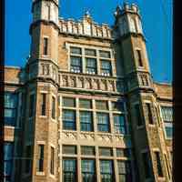          Color slide of close-up view of façade, brick turrets, parapet, and frieze reading 