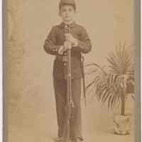 Cabinet photo of ca. 8-10 years old boy posed in military uniform with rifle in a studio, Hoboken, n.d., ca. 1892-1900.