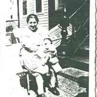 Black-and-white photocopy of photo of Philomina Ratti seated and holding a baby in front of 721 Adams St., Hoboken, 1940.